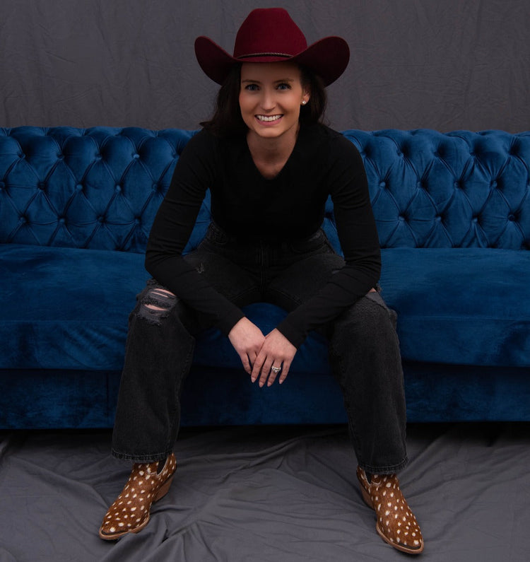 Person wearing a red cowboy hat and black outfit sitting on a blue couch with a gray background